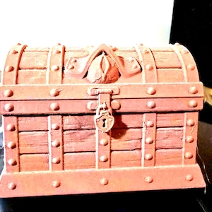 May include: A small, reddish-brown wooden treasure chest with metal accents. The chest has a curved top, a hinged lid, and a decorative lock. The exterior features horizontal planks and metal studs.