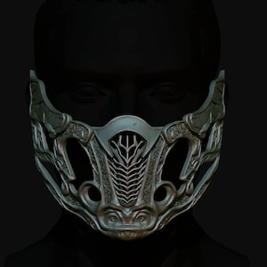 May include: A detailed, silver-coloured mask with intricate designs and a geometric pattern. The mask covers the nose and mouth and has a stylised, almost animalistic face.