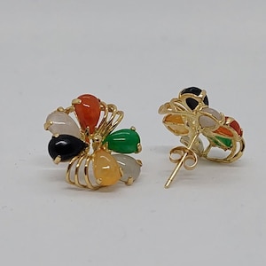 May include: A pair of gold earrings with a flower design. The earrings feature five different colored gemstones: white, black, orange, yellow, and green.