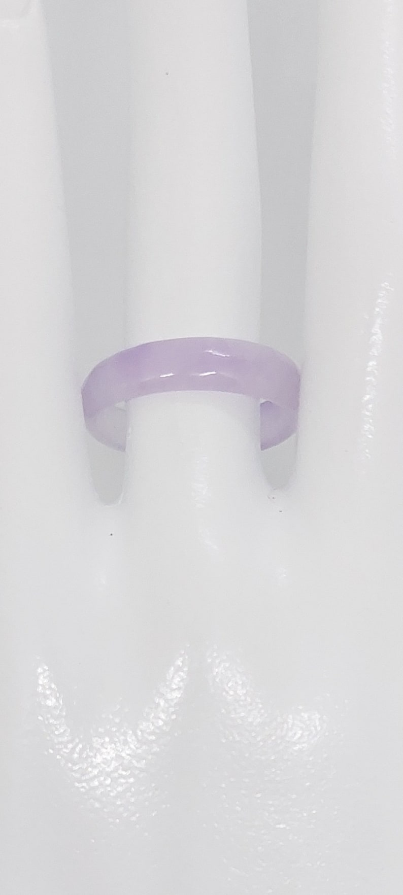 K&ouml;nnte beinhalten: Ein schlichter, helllila Ring aus glattem, poliertem Material. Der Ring wird auf einer wei&szlig;en Mannequin-Hand gezeigt.