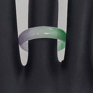 K&ouml;nnte beinhalten: Ein gr&uuml;ner, wei&szlig;er und lilafarbener Jade-Ring. Der Ring wird auf einem schwarzen Handmodell gezeigt.
