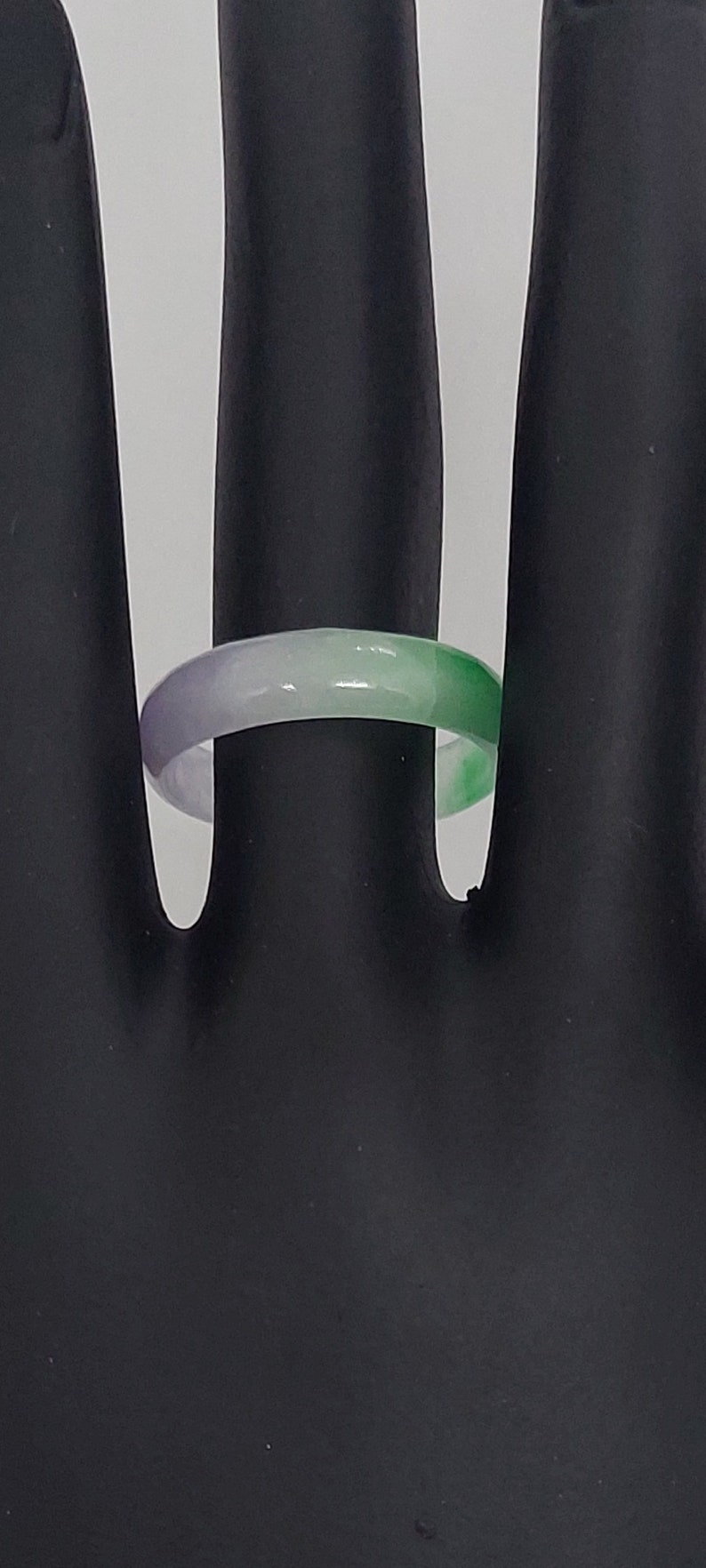 K&ouml;nnte beinhalten: Ein gr&uuml;ner, wei&szlig;er und lilafarbener Jade-Ring. Der Ring wird auf einem schwarzen Handmodell gezeigt.
