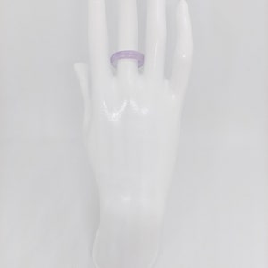 K&ouml;nnte beinhalten: Ein Ring aus Jade in Lavendelfarbe. Der Ring befindet sich an einer wei&szlig;en Mannequin-Hand.
