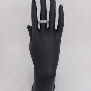 K&ouml;nnte beinhalten: Ein einfacher Jade-Ring mit einem gr&uuml;n-violetten Farbverlauf. Der Ring befindet sich an einem schwarzen Handmodell.