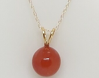 May include: A silver chain necklace with a gold pendant featuring a round, red gemstone.