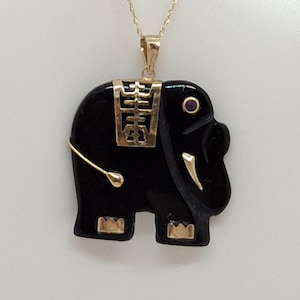 May include: A gold chain necklace with a black onyx elephant pendant. The elephant has gold accents and a small red stone for an eye.