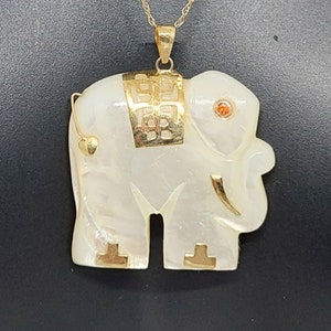 May include: A gold chain necklace with a white mother of pearl elephant pendant. The elephant has gold accents and a small red gemstone for an eye.