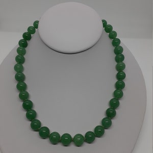 May include: A green jade bead necklace with a simple design. The necklace is made of round beads that are strung together on a thin cord. The beads are a light green color and have a smooth, polished finish.