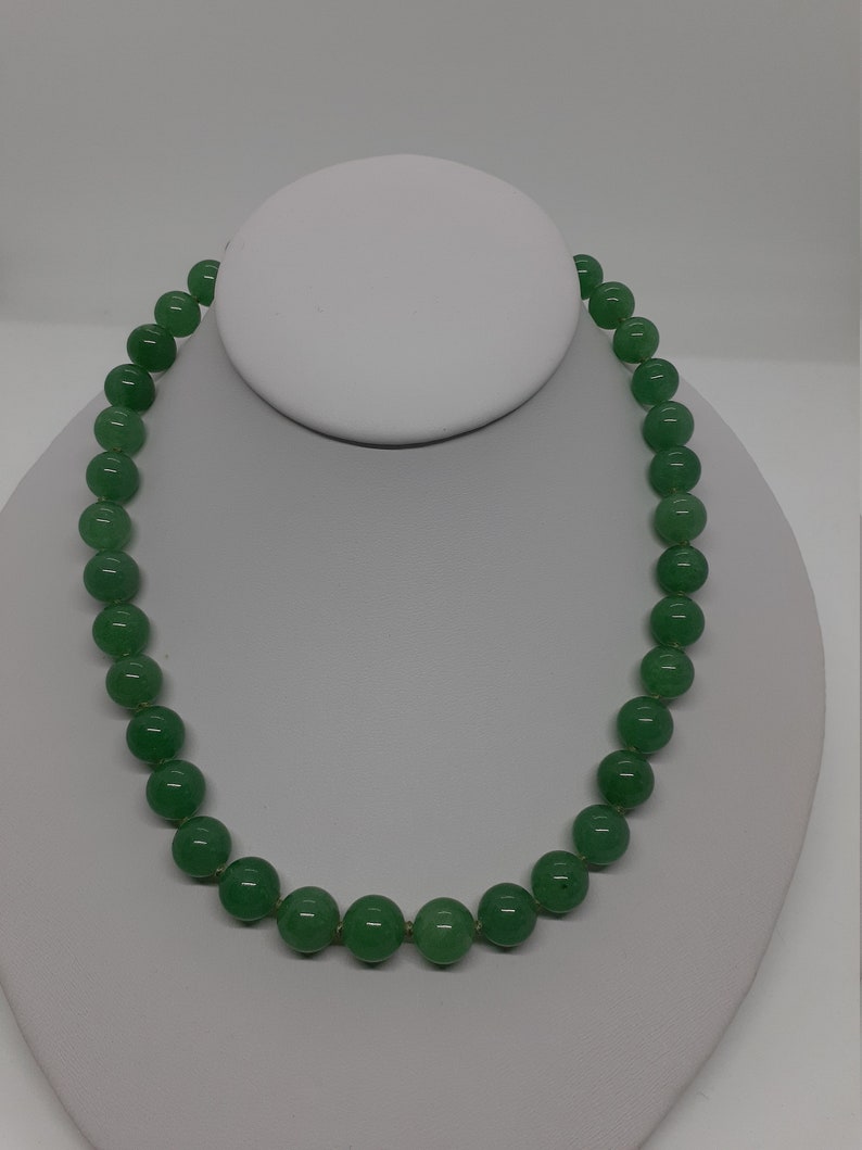 May include: A green jade bead necklace with a simple design. The necklace is made of round beads that are strung together on a thin cord. The beads are a light green color and have a smooth, polished finish.