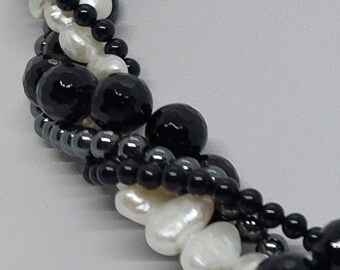 Puede incluir: Un collar de múltiples hilos con cuentas negras, blancas y grises. El collar está hecho de perlas, ónix y hematites.