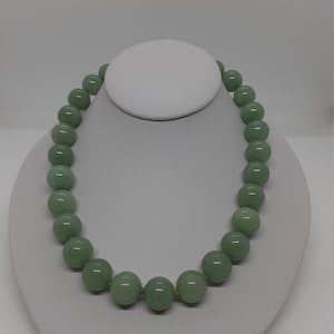 May include: A green jade bead necklace with round beads. The necklace is on a white display stand.