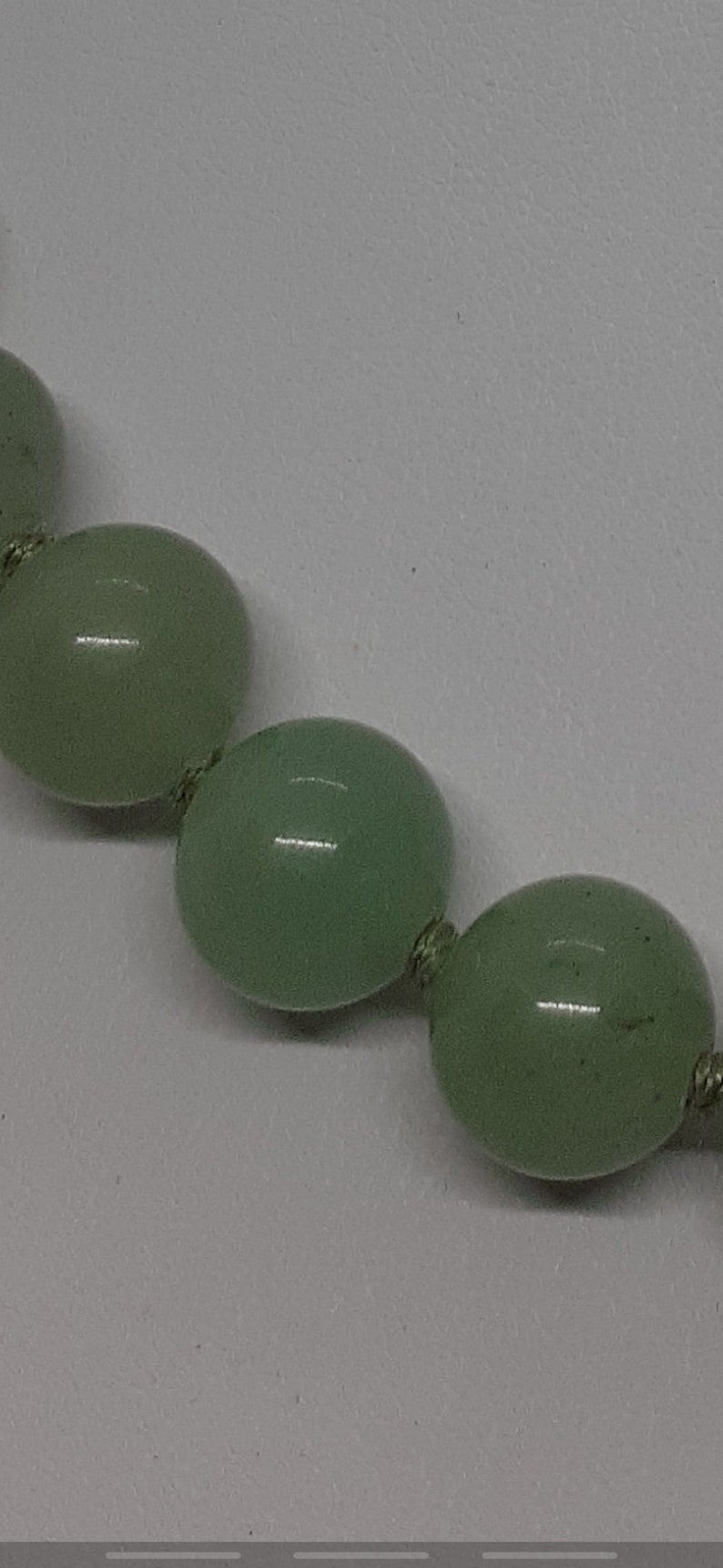 May include: A strand of light green jade beads with a knotted string.