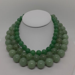 May include: A three-strand necklace made of green jade beads. The beads are round and smooth, and they are graduated in size, with the largest beads at the bottom of the necklace.
