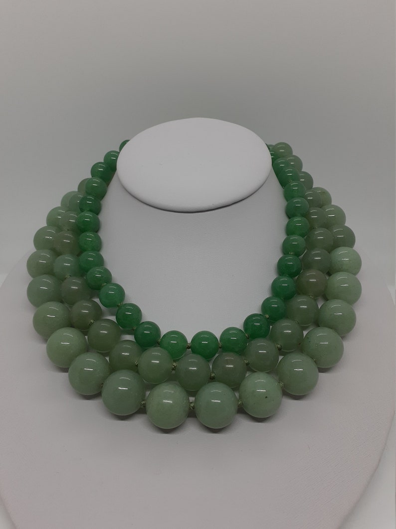 May include: A three-strand necklace made of green jade beads. The beads are round and smooth, and they are graduated in size, with the largest beads at the bottom of the necklace.