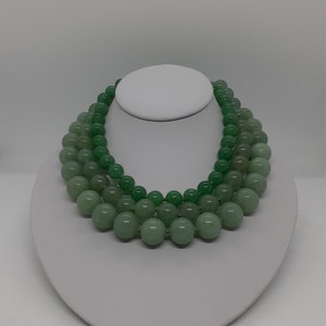 May include: A three-strand necklace made of light green jade beads. The beads are round and smooth, and the necklace is displayed on a white mannequin bust.
