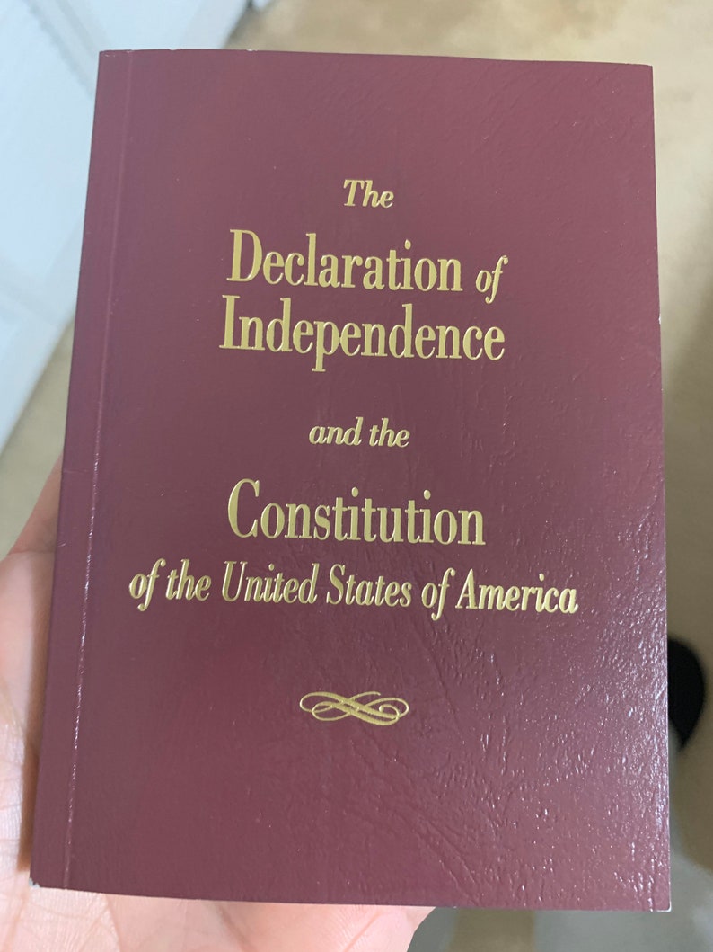 May include: A burgundy-colored book with gold lettering on the cover. The title reads "The Declaration of Independence and the Constitution of the United States of America".
