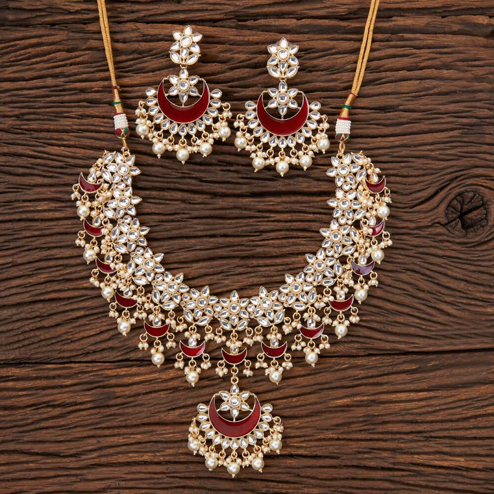 Ornate Kundan necklace set featuring rich crimson crescent meenakari accents, intricate floral clusters, pearl drops, and matching chandbali