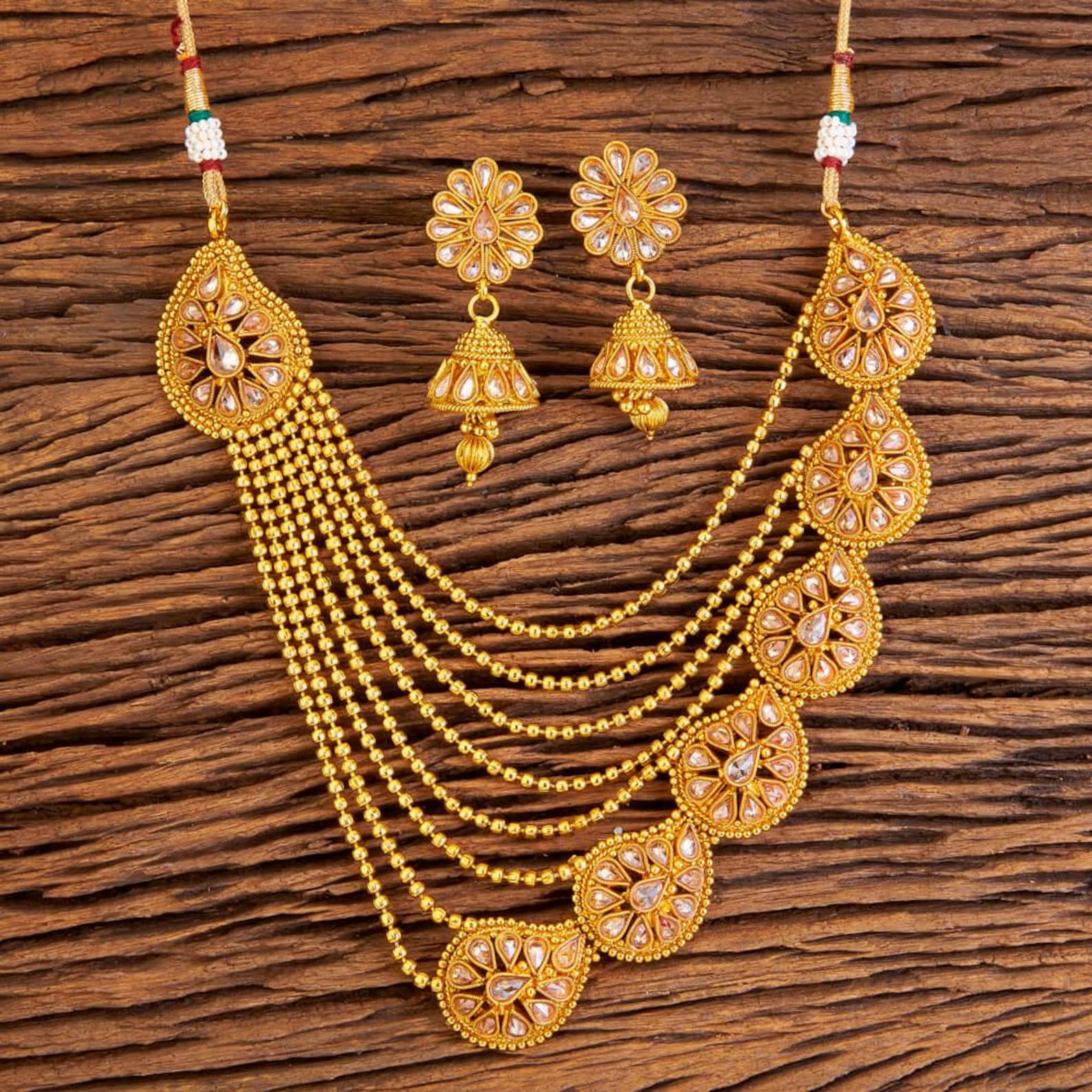 An elegant gold-toned multi-strand beaded necklace set with Kundan-studded floral teardrop motifs and matching traditional jhumka earrings.