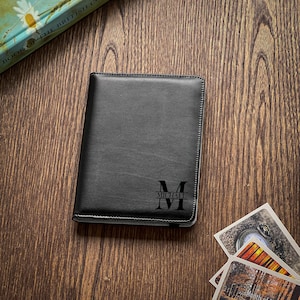 Może przedstawiać: Czarny skórzany notes z personalizowanym monogramem. Monogram to duża litera "M" z napisem "MICHAEL" poniżej.