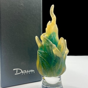 Op de afbeelding: Een groene en gele glassculptuur van een vlam op een heldere glazen voet. De sculptuur is gesigneerd "Daum France".