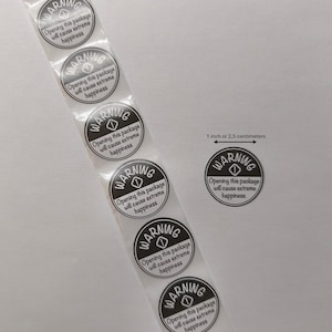 May include: A strip of round stickers with the word "WARNING" in a black circle, with the text "Opening this package will cause extreme happiness." The stickers are approximately 1 inch in diameter.