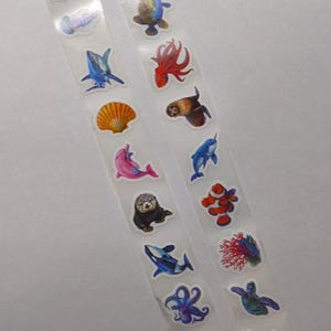 Peut inclure: Deux bandes d'autocollants transparents représentant diverses créatures marines. Les autocollants comprennent une méduse, un requin, un coquillage, un dauphin, une loutre de mer, une baleine, une pieuvre, une tortue, etc. Les autocollants sont colorés et détaillés.