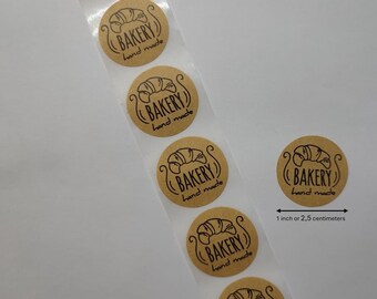 May include: Roll of 1 inch round brown kraft paper stickers with a black and white illustration of a croissant and the text "BAKERY hand made".