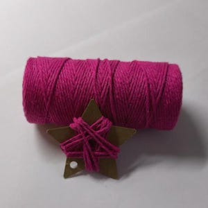 Op de afbeelding: Een rol levendig fuchsia-kleurig touw ligt naast een kleine, bruine kartonnen ster, gewikkeld met bijpassend touw. Het touw is strak gewikkeld en de ster heeft een klein gaatje. Geschikt voor knutselprojecten.