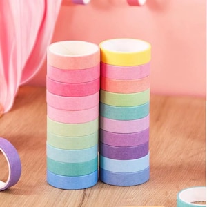 Op de afbeelding: Twee verticale stapels met kleurrijke washi-tape rollen in diverse pasteltinten zoals roze, geel, groen, blauw en paars. Elke rol heeft een effen matte afwerking met een witte kartonnen kern, netjes gerangschikt op een houten ondergrond.