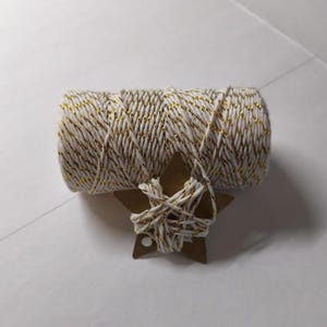 Peut inclure: Une bobine de ficelle blanche et dorée avec une petite étiquette en forme d'étoile marron. La ficelle est enroulée autour de l'étiquette. La ficelle est un élément décoratif pour l'artisanat, l'emballage de cadeaux ou d'autres projets créatifs.