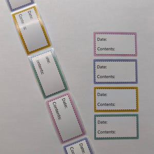 Könnte beinhalten: Rechteckige Etiketten mit dem Text "Datum:" und "Inhalt:" in einer weißen Box. Die Etiketten haben farbige Ränder in Rosa, Blau, Gelb und Grün. Die Etiketten sind auf einer Rolle und auch einzeln.
