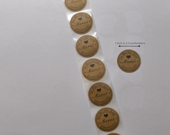 May include: A strip of round, brown stickers with the word "Merci" and a heart symbol. Each sticker is approximately 1 inch in diameter. The text "Fait Avec Amour" is printed around the edge of the stickers. The stickers are on a clear backing.