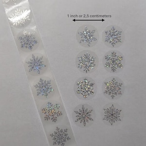 Op de afbeelding: Ronde, transparante stickers met zilveren sneeuwvlokontwerpen. De tekst luidt "1 inch or 2,5 centimeter". De sneeuwvlokken hebben een holografisch effect. Geschikt voor knutselen of feestversieringen.
