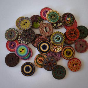 Może przedstawiać: Zestaw kolorowych drewnianych guzików z misternymi wzorami mandali. Guziki są okrągłe i mają po dwa otwory.