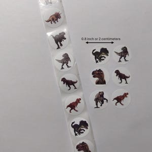 Op de afbeelding: Een rol ronde stickers met verschillende dinosaurusillustraties in bruin, rood en zwart. De tekst op de afbeelding luidt "0,8 inch of 2 centimeter".