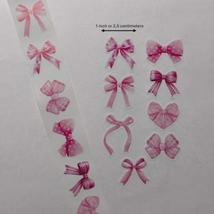 Pode incluir: Uma coleção de autocolantes de laço rosa em vários designs, incluindo bolinhas e padrões listrados. Os autocolantes estão dispostos numa tira transparente e individualmente. O texto na imagem diz "1 polegada ou 2,5 centímetros".