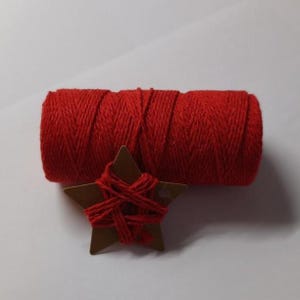 Peut inclure: Un rouleau de ficelle rouge vif à côté d'une étiquette en forme d'étoile marron, également ornée de ficelle rouge. La ficelle est bien enroulée, et l'étiquette en forme d'étoile comporte un petit trou. Sur fond blanc.