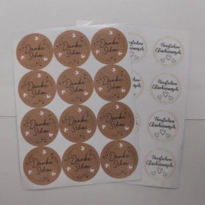 Puede incluir: Hojas de pegatinas redondas con texto en alemán. Las pegatinas marrones dicen "Danke Schön" con un diseño de corazón y pájaro. Las pegatinas blancas dicen "Herzlichen Glückwunsch" con corazones.