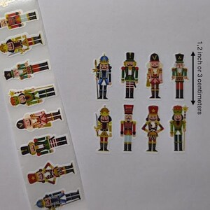 May include: A sheet of colourful nutcracker stickers. The stickers feature various nutcracker designs in red, green, blue, and gold. The height of the nutcrackers is 3 centimetres.