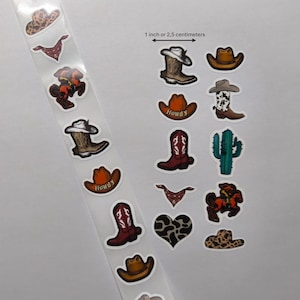 May include: A selection of cowboy-themed stickers, featuring cowboy hats, boots, bandanas, and a cactus. The stickers are in various colours and patterns, with some displaying the word "Howdy". The image includes a measurement of 2.5 centimetres.