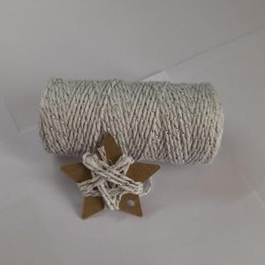 Könnte beinhalten: Eine Rolle silber-weißes Garn mit metallischen Akzenten, neben einem braunen Pappstern, der mit dem gleichen Garn umwickelt ist. Das Garn ist fest gewickelt und der Stern hat ein Loch zum Aufhängen. Ideal zum Basteln und Geschenkverpacken.