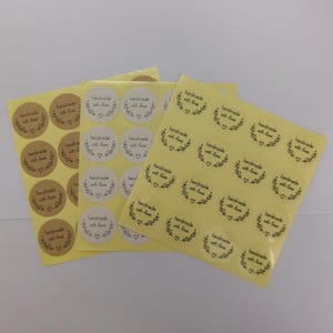 Può includere: Fogli di adesivi rotondi con la scritta "handmade with love" in un carattere scritto a mano. Gli adesivi sono in vari colori, tra cui marrone kraft e giallo chiaro. Ogni adesivo presenta un disegno a ghirlanda.