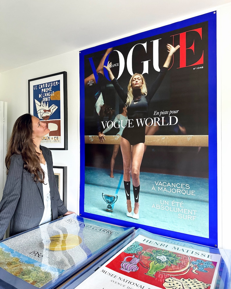 May include: A Vogue magazine cover featuring a woman in a black leotard performing a gymnastics pose on a balance beam. The cover is blue and red with the text "Vogue World" and "Vacances a Majorque Un Ete Absolument Surf".
