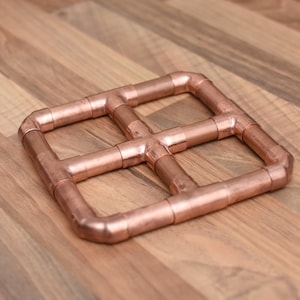 May include: A square copper pipe coaster with a grid pattern. The coaster is made of multiple copper pipes joined together.