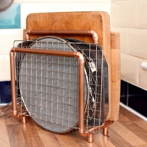 May include: Copper pipe rack with a wooden chopping board, a metal baking sheet, and a round metal rack.