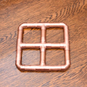 May include: A copper pipe grid with a square shape. The grid is made of four copper pipes that are connected together at the corners and in the middle. The grid is a decorative piece that can be used for a variety of purposes.
