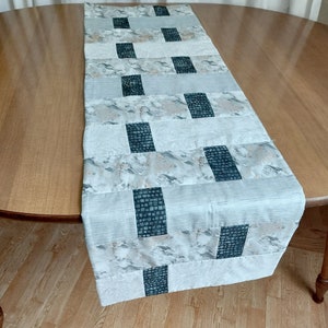 May include: A white table runner with a geometric pattern of black squares. The runner has a subtle marbleized effect and is made of a soft, textured fabric.