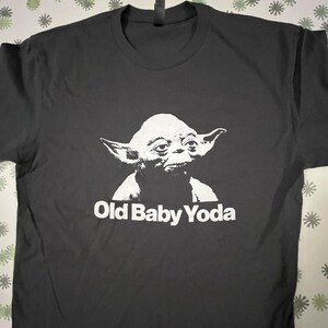 May include: Black t-shirt with a white image of Yoda from Star Wars and the text "Old Baby Yoda".