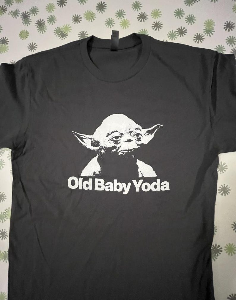 May include: Black t-shirt with a white image of Yoda from Star Wars and the text "Old Baby Yoda".