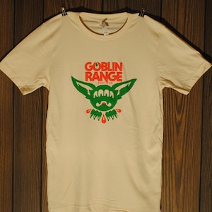 May include: A cream colored t-shirt with a green and red goblin graphic. The graphic says "Goblin Range Print Co."